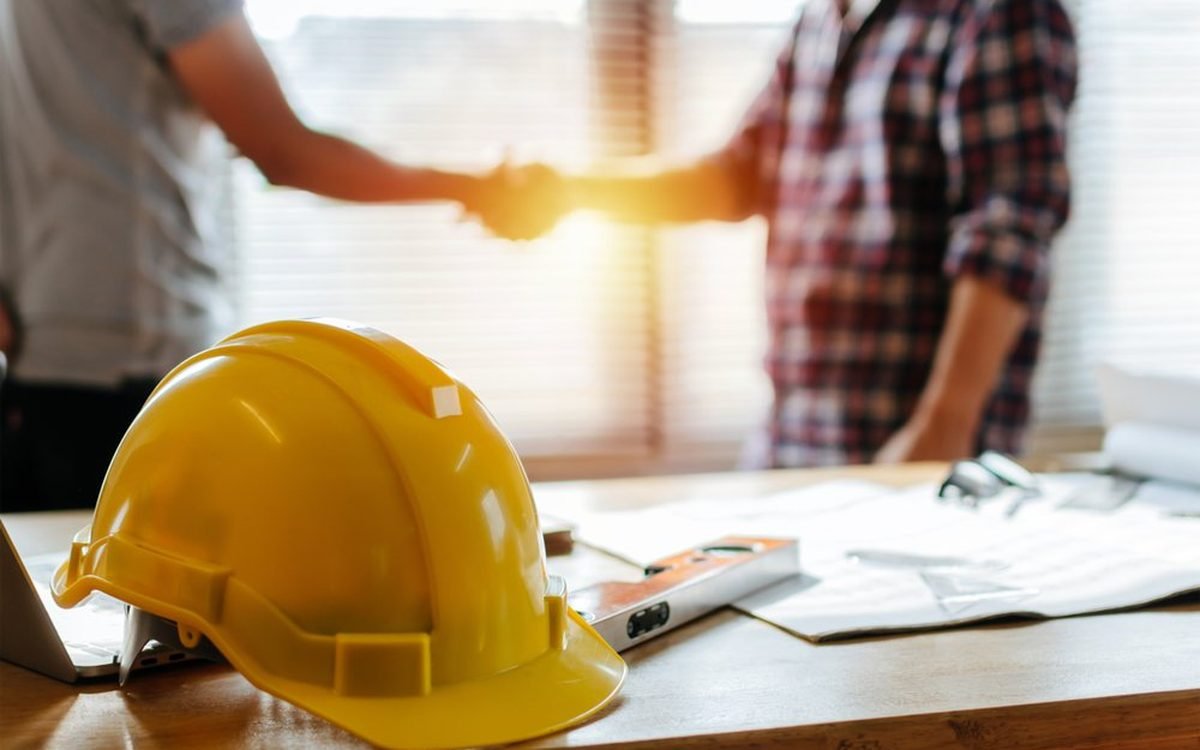 Contractor shaking hands with a client over blueprints and a hard hat